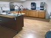 A small food service area with a wooden floor, featuring an empty buffet counter, beverage dispensers, and wooden cabinets along the walls.