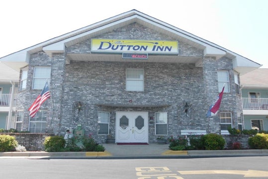 Front view of a two-story brick building with a sign reading "Dutton Inn" and a "Vacancy" notice. U.S. and state flags are displayed.