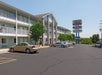 A three-story motel with parked cars in the lot, featuring a sign for "Dayton's Inn" and "Dayton Deli" against a clear sky.