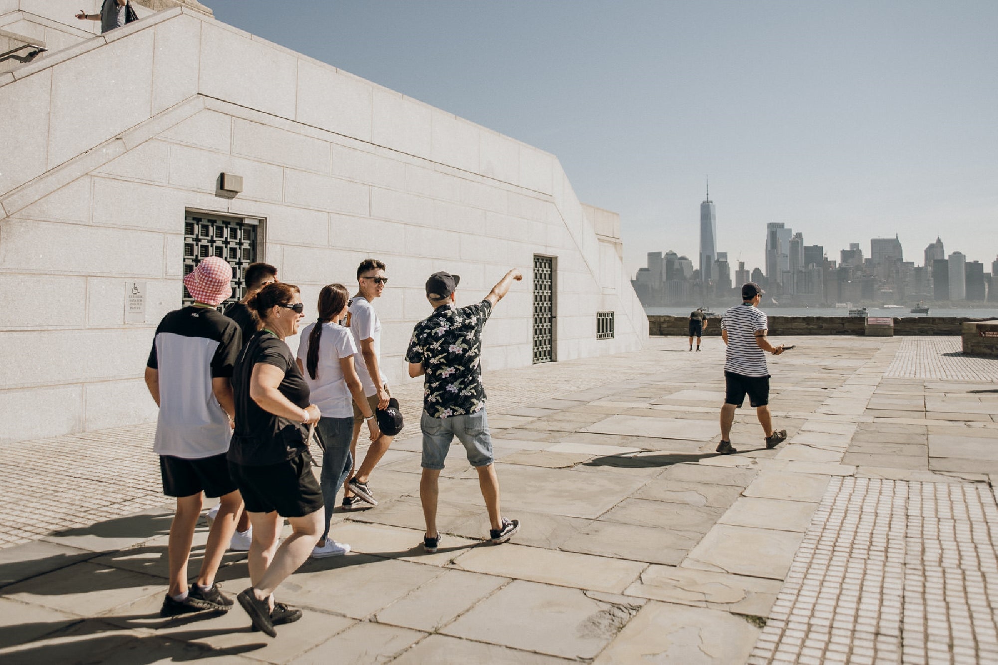 A group of people stand on a stone terrace with one person pointing towards a city skyline in the background on a clear day.