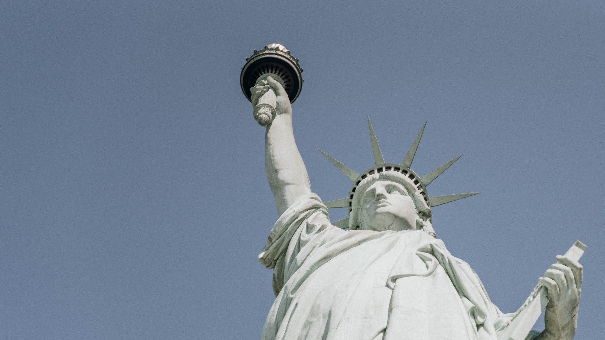 The Statue of Liberty against a clear blue sky, with the torch held high in its right hand.