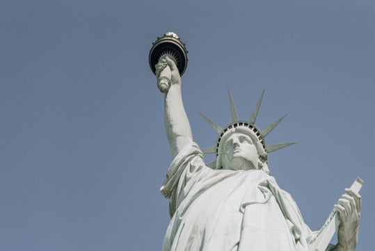 The Statue of Liberty holding a torch aloft in her right hand and a tablet in her left, set against a clear blue sky.