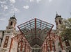 A historic building with two towers and a large glass and red metal canopy at the entrance, set against a partly cloudy sky.