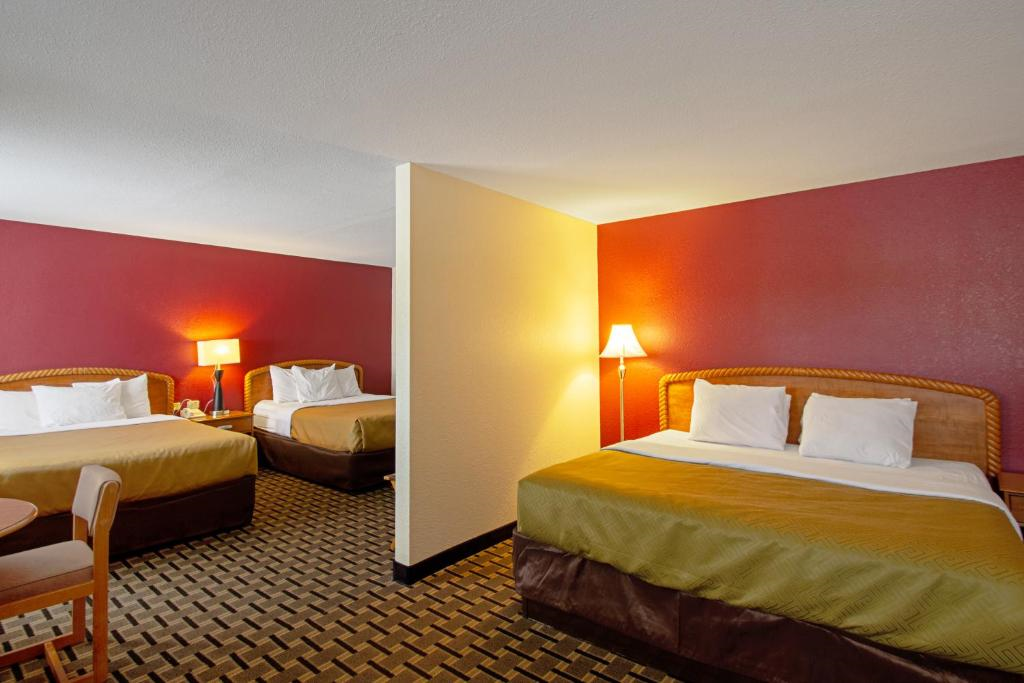 Hotel room with two double beds, red walls, and patterned carpet. A lamp and table with chairs are also present.