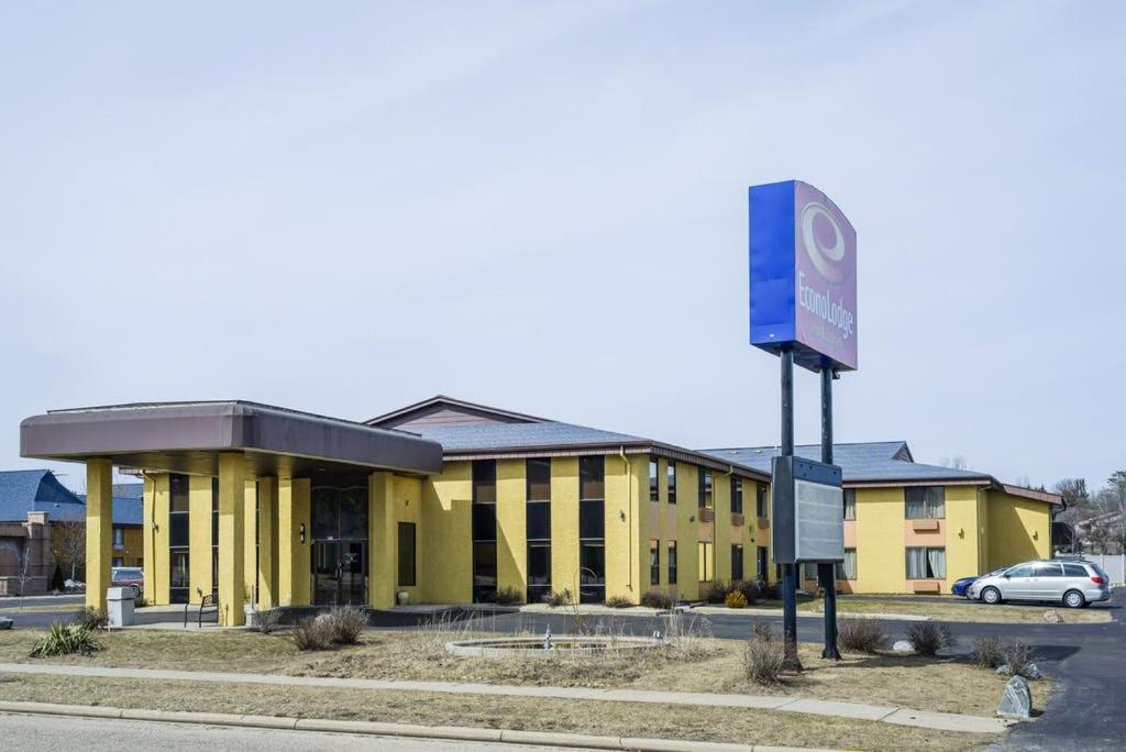 A two-story yellow building with a covered entrance and a purple and white sign in the parking lot under a clear sky.