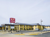 Econo Lodge building with a parking lot in front, featuring a large red sign and several parked cars. The sky is clear and the area appears quiet.
