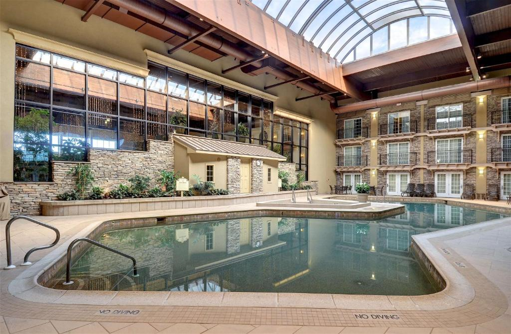 Indoor pool area with a wooden ceiling and large windows. The pool is surrounded by a stone facade and potted plants. Signs indicate "No Diving.