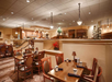 Empty restaurant with wooden tables and chairs, set with cups and napkins. Subdued lighting and warm decor create a cozy atmosphere.