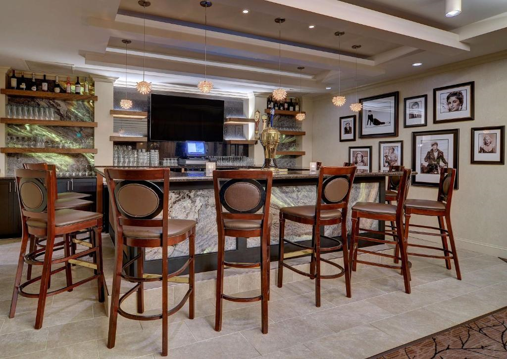A modern home bar with high wooden chairs, a granite counter, pendant lights, and framed photos on the walls.