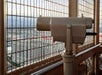 A coin-operated binocular viewer is mounted on an observation deck, overlooking tall buildings and a cityscape through a metal safety fence.