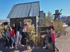 A group of people pose in front of a rustic building with a "Pin-Ups" sign. Desert landscape, cacti, and vintage items are in the background.