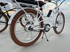 White electric bicycles with brown tires parked on a sandy beach, facing the ocean under a cloudy sky.