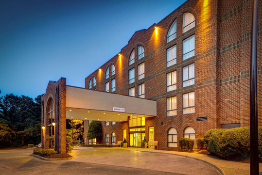 Exterior of a brick hotel building with arched windows and an entrance canopy, illuminated at dusk.
