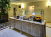 Buffet setup with a variety of fruits, salads, and plates on a wooden counter in a well-lit dining area.
