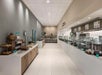 Empty cafeteria with modern decor, counters on both sides, display items on the left, and food stations on the right. Neutral color palette and tiled floor.