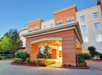 Entrance of a hotel with a terracotta archway, surrounded by landscaping, under a clear blue sky.