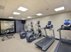 A gym with treadmills, stationary bikes, benches, and weightlifting equipment under fluorescent lighting.