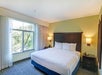 Hotel room with a large bed, two bedside tables with lamps, and a window with curtains overlooking trees.