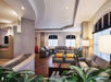 A modern living room with gray sofas, plants, large windows, and white brick walls, illuminated by soft lighting.