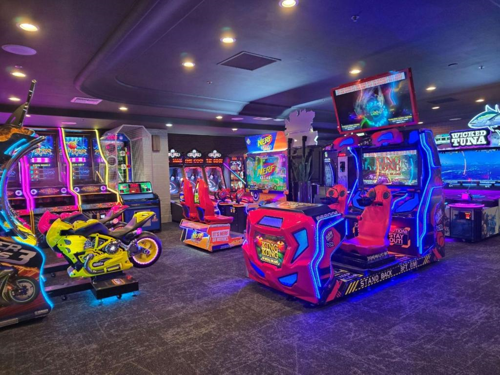 A vibrant arcade room filled with various colorful gaming machines and racing simulators under dim lighting.