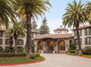 Hotel exterior surrounded by trees and a fountain at front.