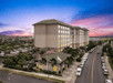 Aerial view of a multi-story hotel at sunset, with cars parked along the street and an American flag outside.