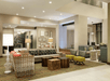 A modern hotel lobby with woven sofas, patterned cushions, green chairs, tables, and framed art on the walls. Bright lighting and a striped carpet enhance the contemporary decor.