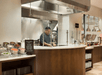 Chef preparing food at a restaurant cooking station with a variety of ingredients and dishes displayed on the counter.