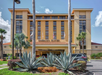Front view of Embassy Suites hotel with tall palm trees, multiple flagpoles, and a neatly landscaped entrance featuring large agave plants.