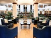 A large hotel lobby with tons of green plants, several circular light fixtures, and a sitting area with blue accent chairs and a round coffee table,