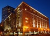 Ground view of the corner of the Embassy Suites by Hilton Portland Downtown at night with lights shining on the building, cars on both sides, and the city in the background.