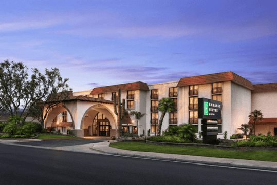 A hotel with a Southwestern architectural style, featuring arches and palm trees, under a purple sky. The sign reads "Embassy Suites.