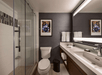 Modern bathroom with a glass shower, large mirror, sink, and toilet. A framed floral picture and folded towels hang on the wall.