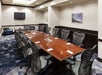 A conference room with a long brown tables with black office chairs around it, a TV on the far wall and a seating area in front of it.