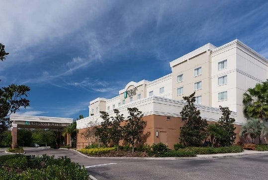 The front exterior of the Embassy Suites by Hilton with several trees in their landscaping on a bright and sunny day.