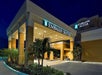 The front exterior and entrance of the the Embassy Suites by Hilton with a covered drive with trees in the landscaping around it at night.