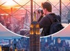 A person with a camera takes photos from an observation deck overlooking New York City with the Empire State Building prominent in the foreground.