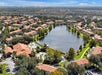 Aerial view of a residential neighborhood with red-roofed buildings surrounding a large lake and swimming pools, with trees and greenery throughout the area.