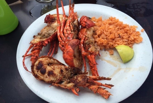 A white plate with grilled lobster halves, a serving of orange rice, and a lime wedge on a dark surface.
