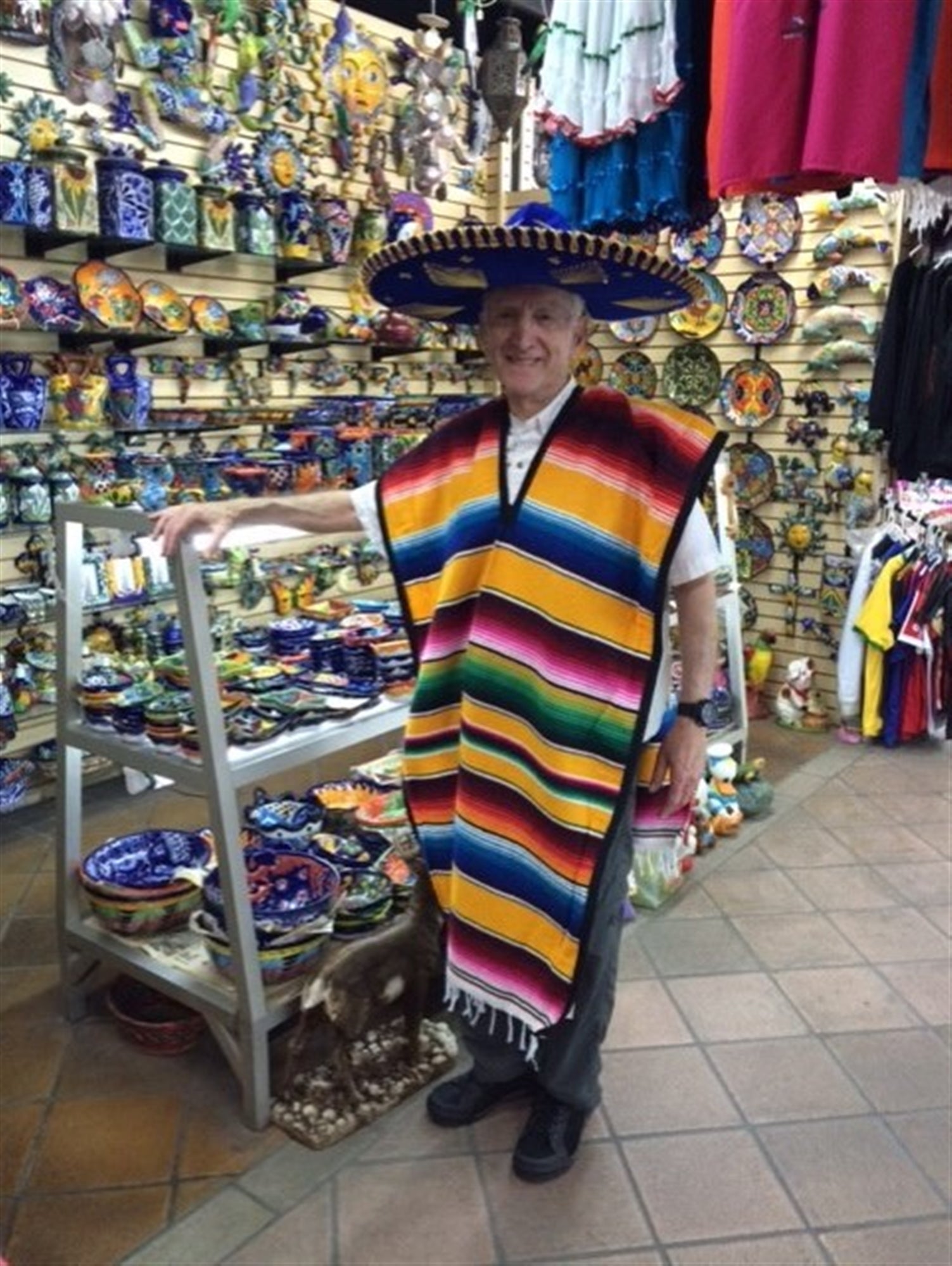 A person wearing a colorful poncho and sombrero stands in a shop filled with Mexican pottery, ceramics, and traditional crafts.