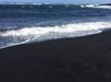 Waves from the ocean roll onto a black sand beach under a clear sky.