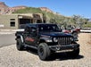 A black Jeep Gladiator park in gravel with red and silver ATVs behind it on a sunny day in Zion National Park.