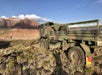 A military vehicle spray painted camouflage parked in a grassy area on a sunny day with the Red Rocks in the background at Zion National Park.