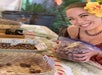 Person smiling while holding a bag of nuts at a table with various nut samples on display.