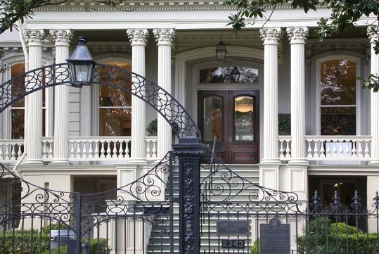 A historic building with a grand entrance featuring tall columns, ornate wrought iron gate, and double wooden doors. The building's facade includes detailed architectural elements and large windows.