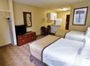 Two double beds, TV, dining table, and fully-equipped kitchen with refrigerator, stovetop, and microwave in a guest room.