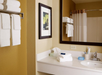 Bathroom interior with a sink, a large mirror, neatly folded white towels on a rack, a framed picture on the wall, and toiletries on the counter.