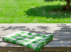 Folded green and white checkered cloth on a wooden table with a grassy background.