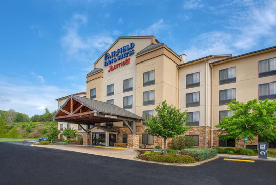 Exterior view of a Fairfield Inn & Suites by Marriott hotel with a stone facade, multiple stories, and landscaped surroundings under a clear blue sky.