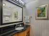 A bathroom with a black countertop, sink, and framed mirror. Towels hang on a rack, and a colorful artwork is on the wall.